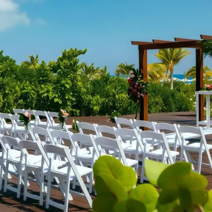 Beach deck wedding ceremony with white chairs and floral arch at Grand Palladium Costa Mujeres, Cancun