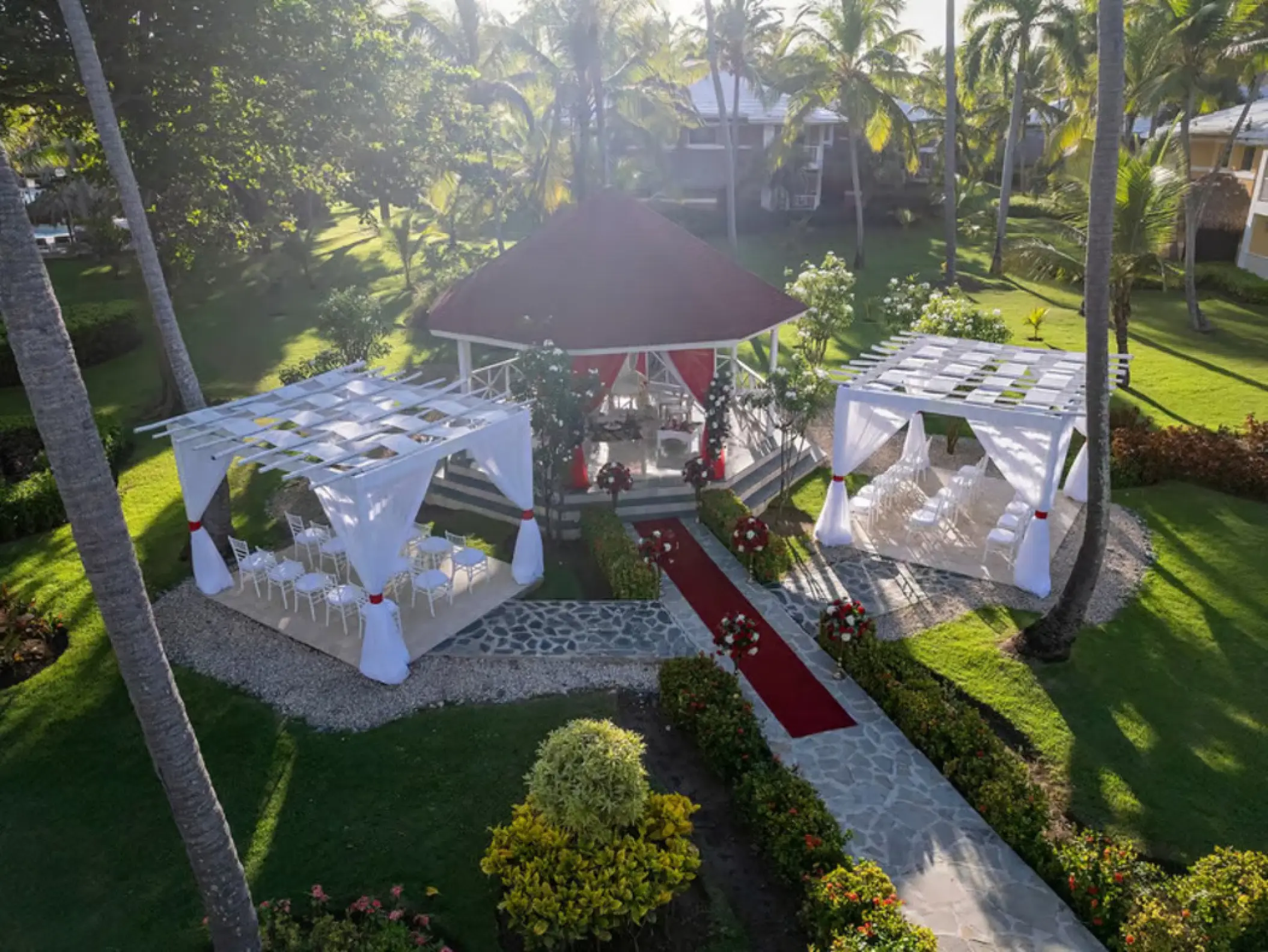Aerial view of a garden wedding ceremony with a red gazebo and white cabanas at Grand Palladium, Punta Cana