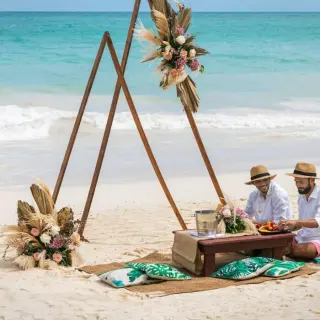 Couple enjoying a beach wedding picnic under a floral triangle arch at Grand Palladium Punta Cana