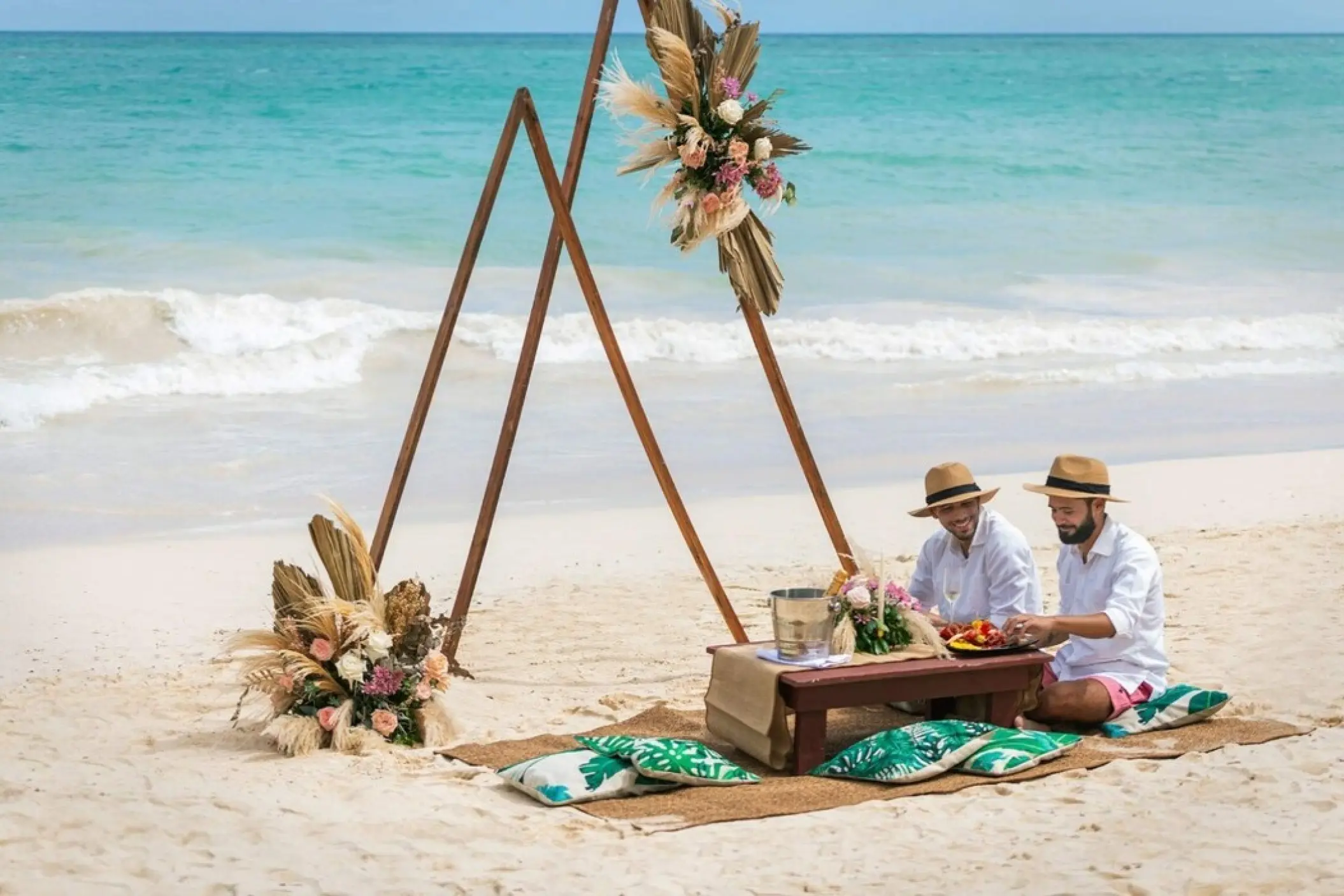 Couple enjoying a beach wedding picnic under a floral triangle arch at Grand Palladium Punta Cana