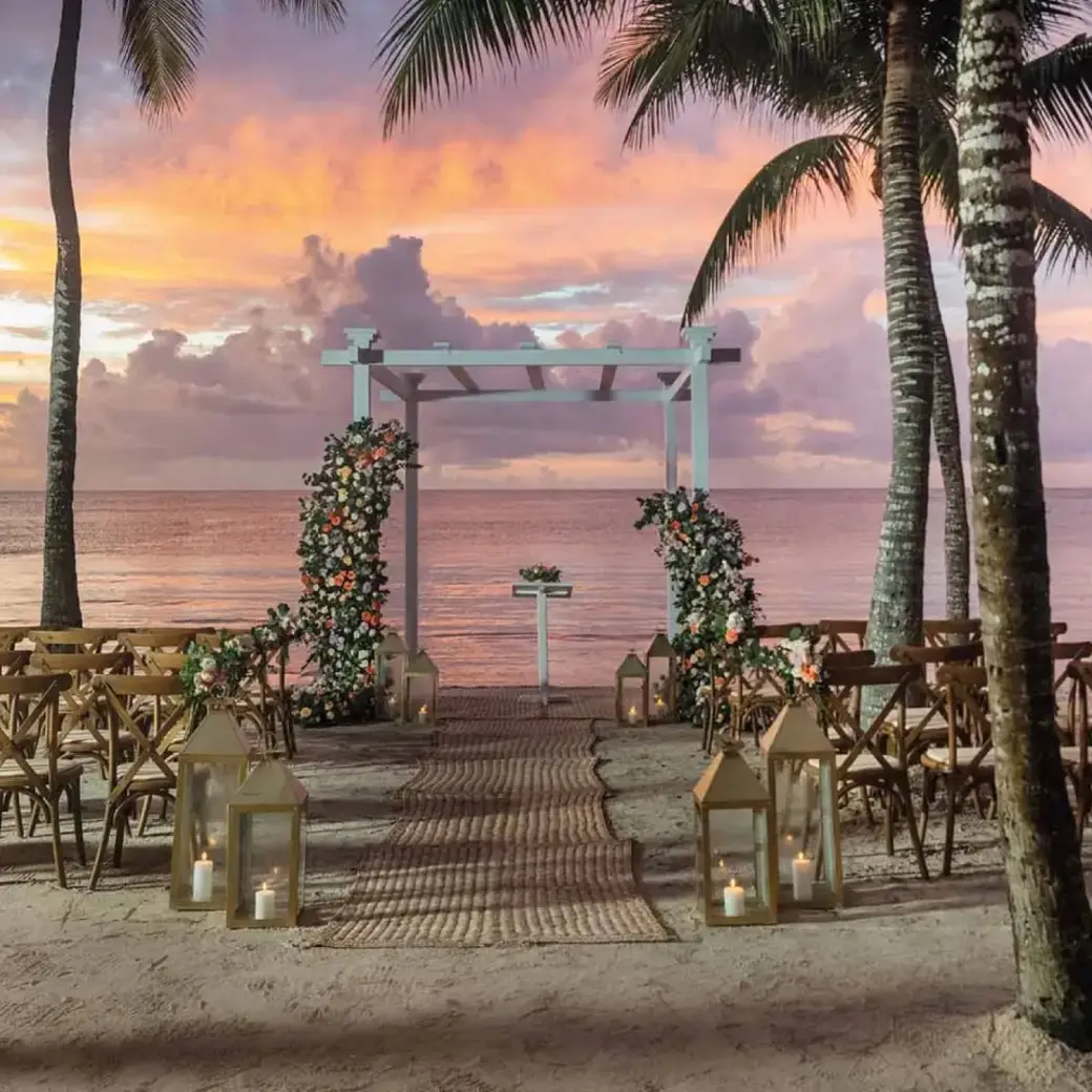 Sunset beach wedding ceremony with wooden chairs and floral arch at Grand Palladium Kantenah, Riviera Maya