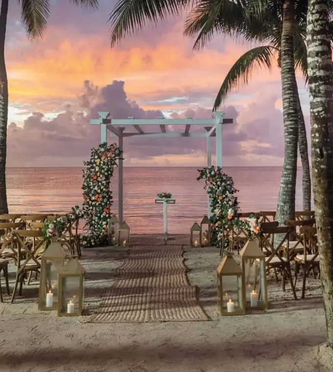 Sunset beach wedding ceremony with wooden chairs and floral arch at Grand Palladium Kantenah, Riviera Maya