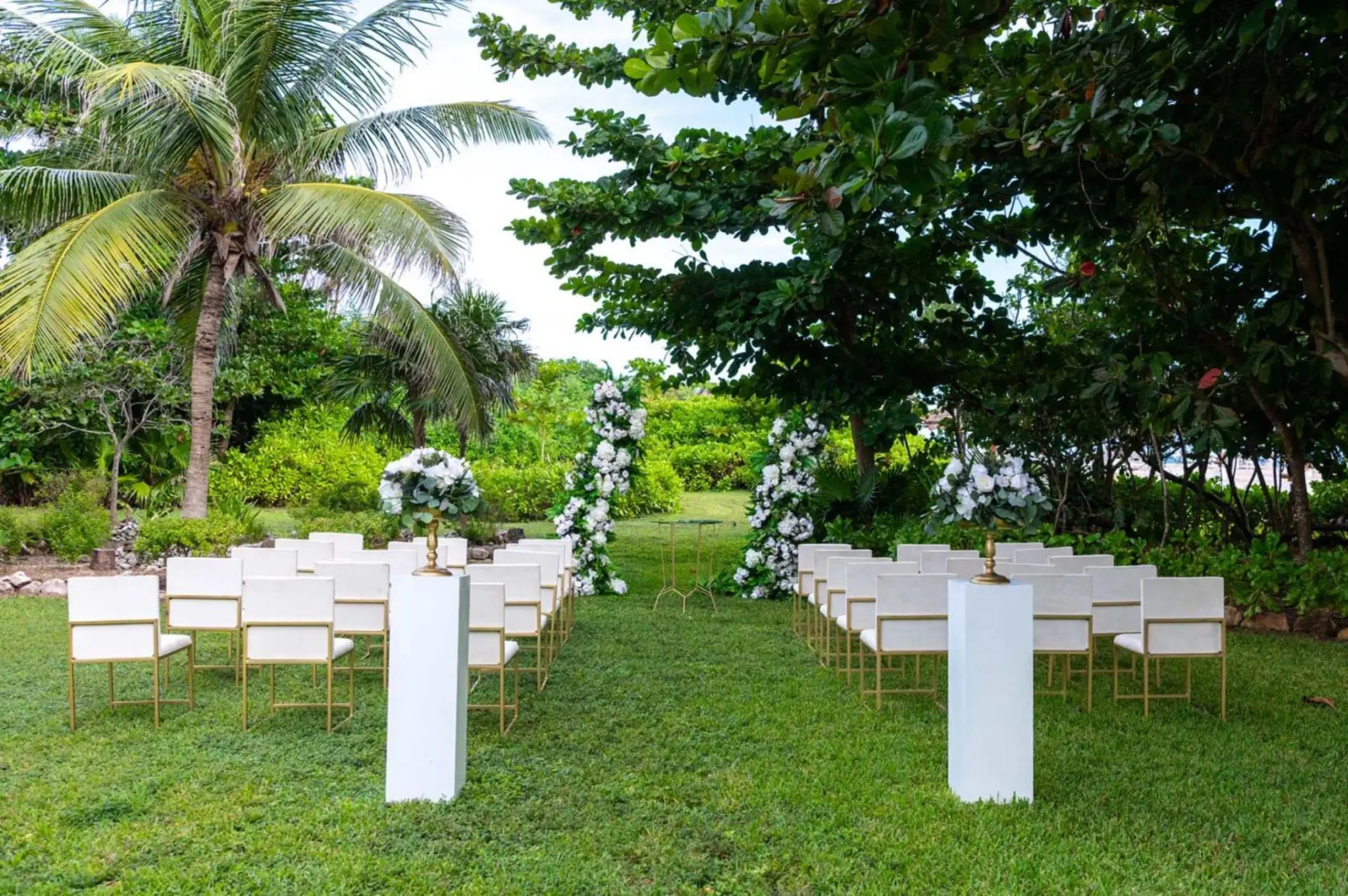 Garden wedding ceremony with white chairs and floral pillars at Grand Sirenis Riviera Maya, Riviera Maya