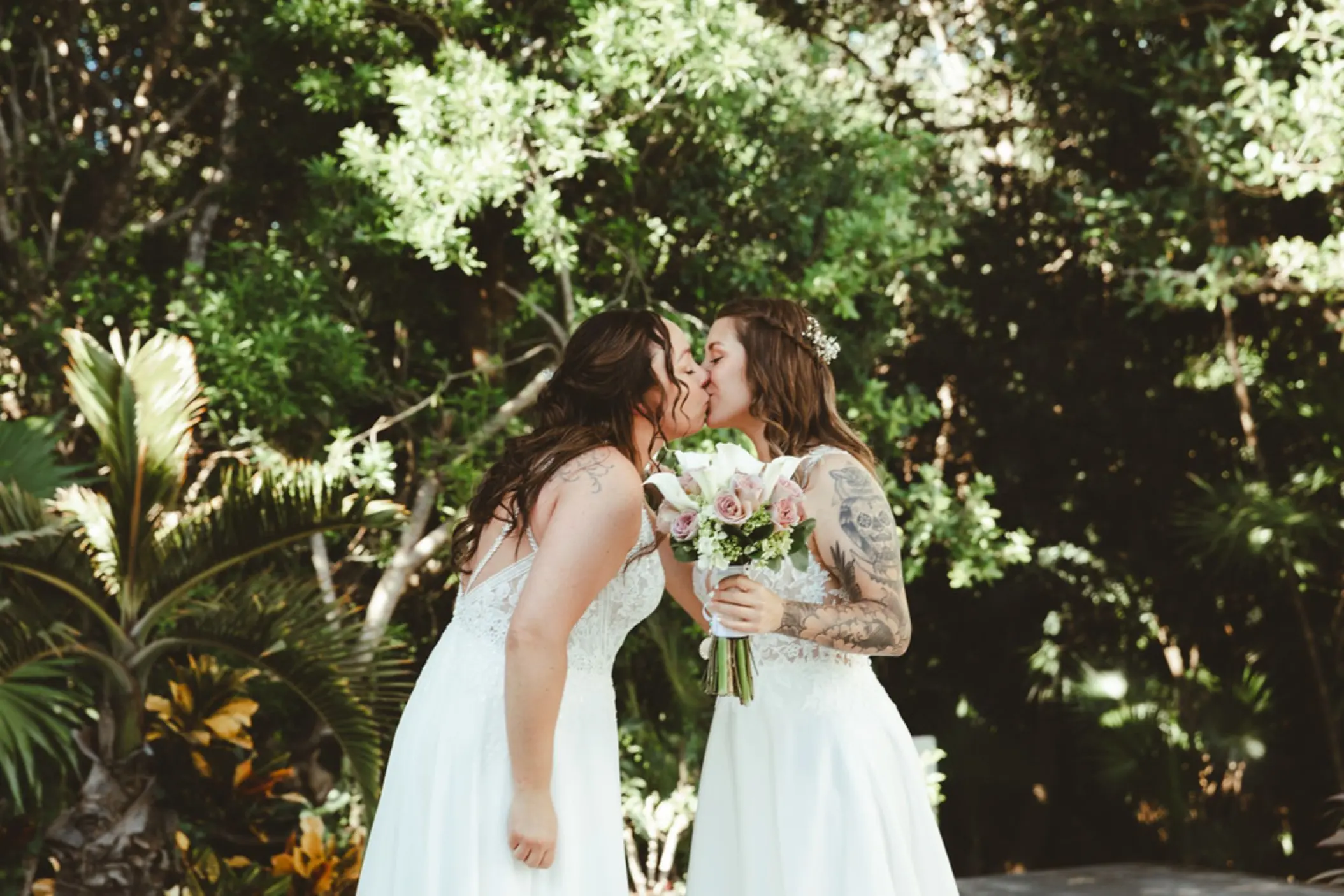 Two brides kissing while holding a flower bouquet at Grand Sirenis, Riviera Maya