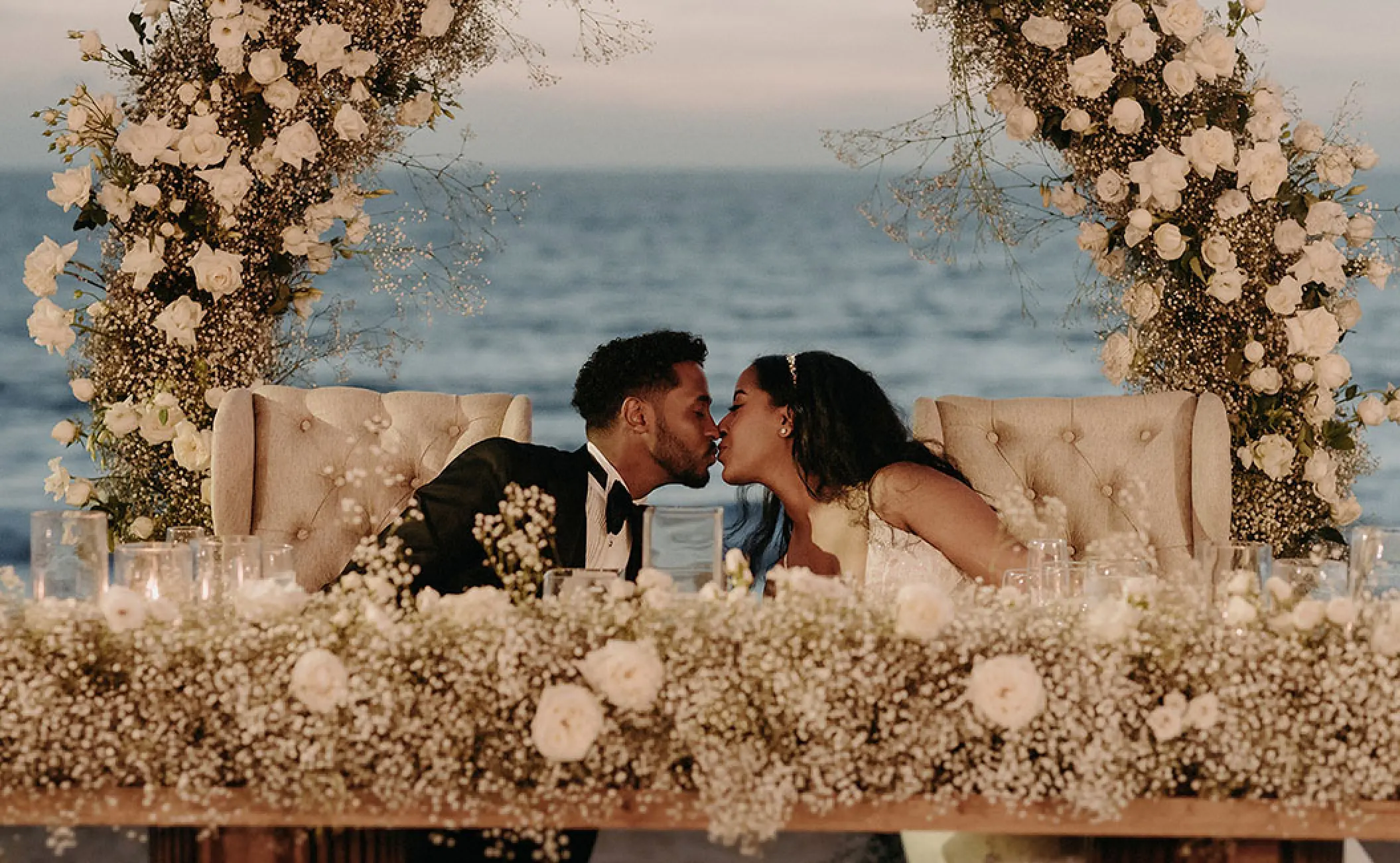 Bride and groom kissing at a floral sweetheart table during their wedding at Grand Velas Riviera Nayarit