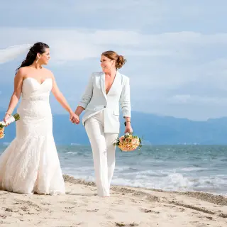Two brides holding hands and walking on the beach at Grand Velas Riviera Nayarit, Puerto Vallarta
