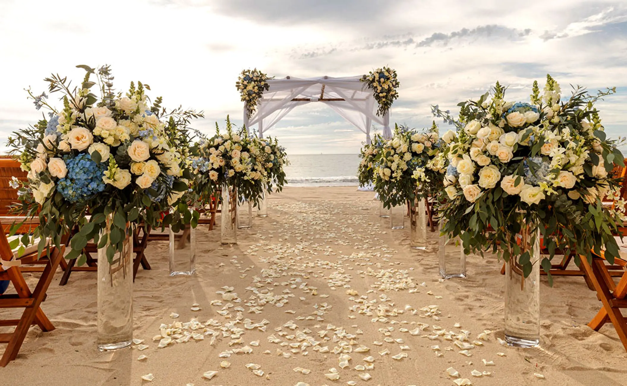 Beachfront wedding ceremony with white flower arrangements and a wooden gazebo at Grand Velas Riviera Nayarit