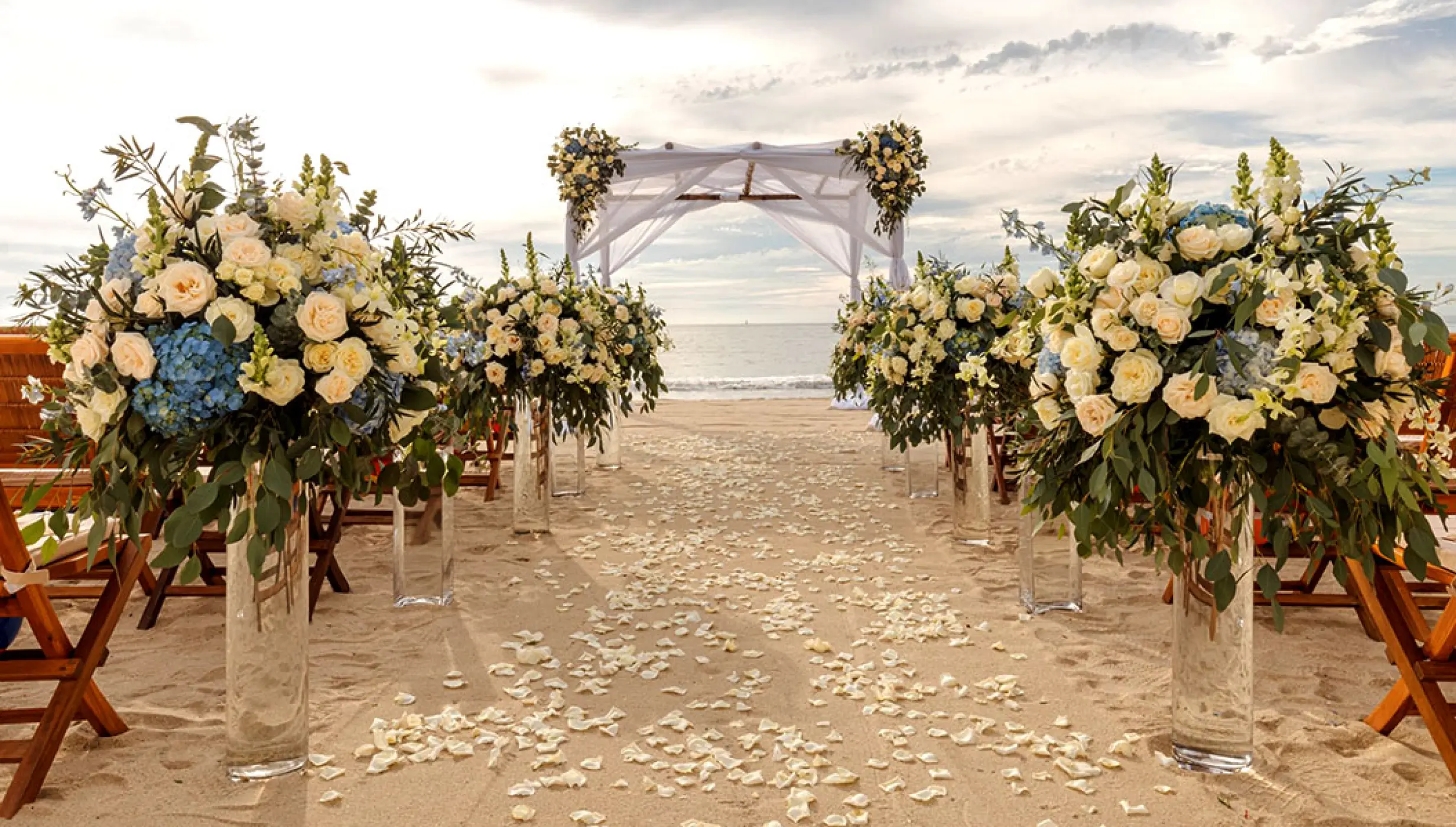 Beachfront wedding ceremony with white flower arrangements and a wooden gazebo at Grand Velas Riviera Nayarit