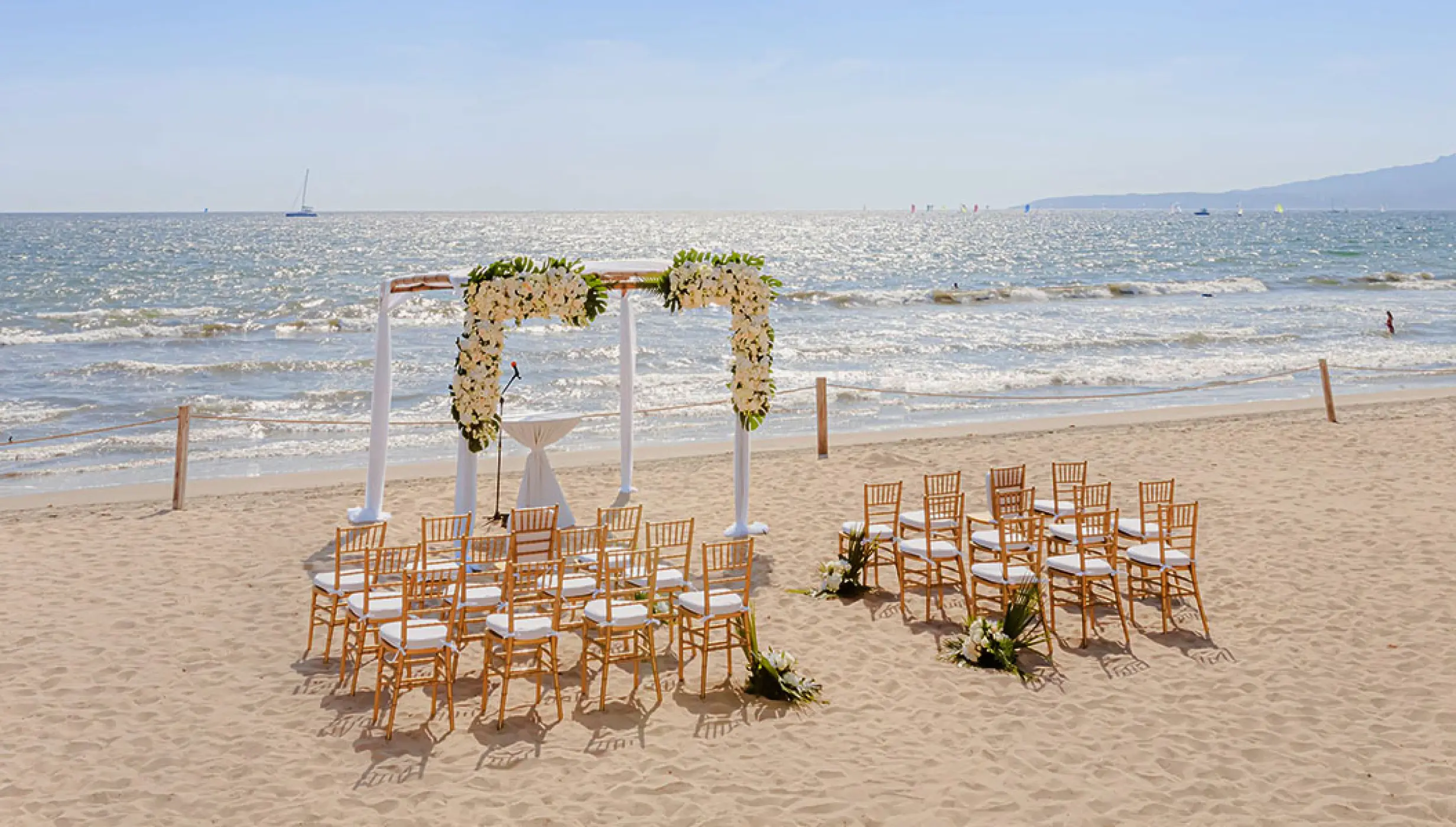 Beachfront wedding ceremony with white flower arch and wooden chairs at Grand Velas Riviera Nayarit, Puerto Vallarta