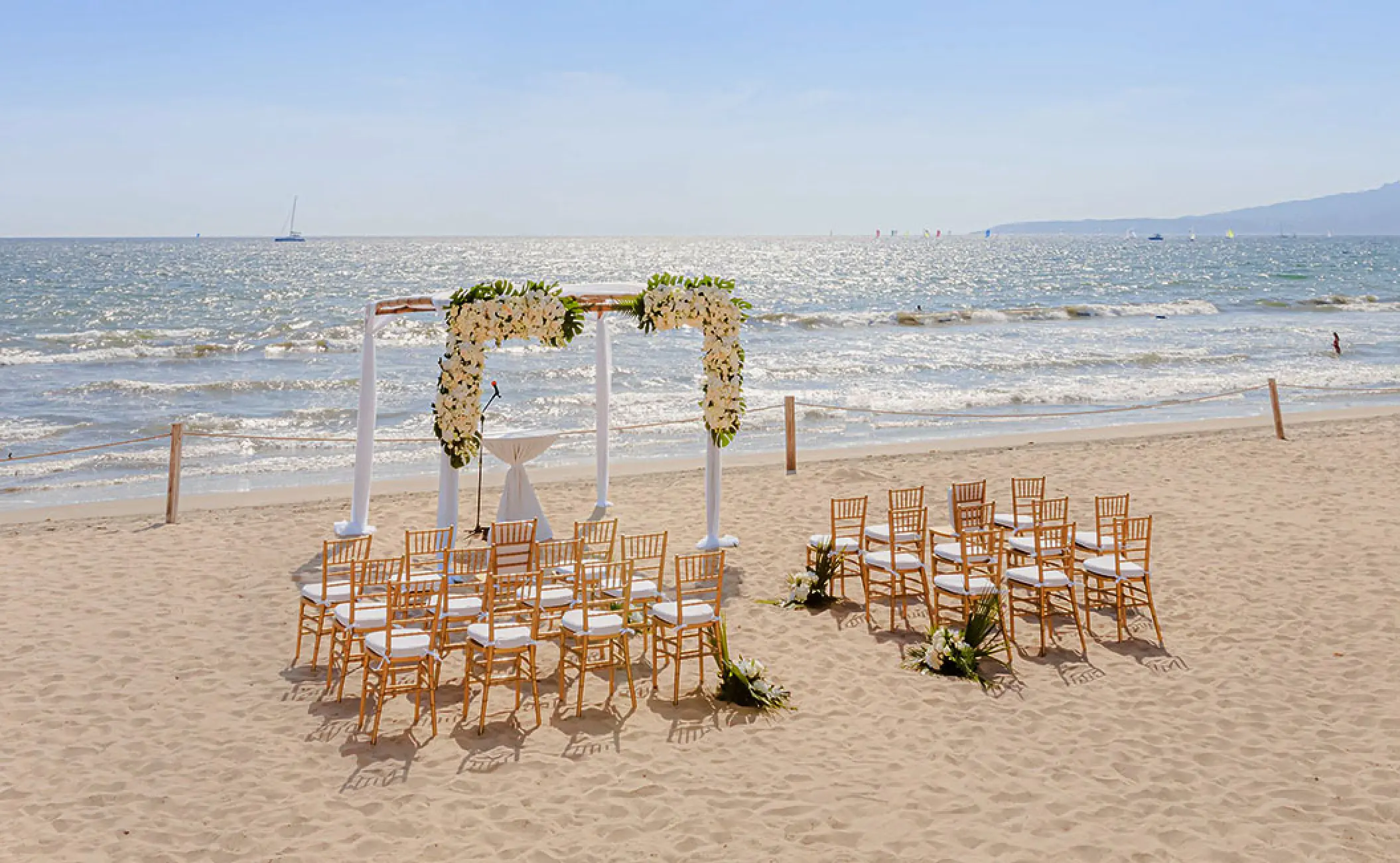 Beachfront wedding ceremony with white flower arch and wooden chairs at Grand Velas Riviera Nayarit, Puerto Vallarta