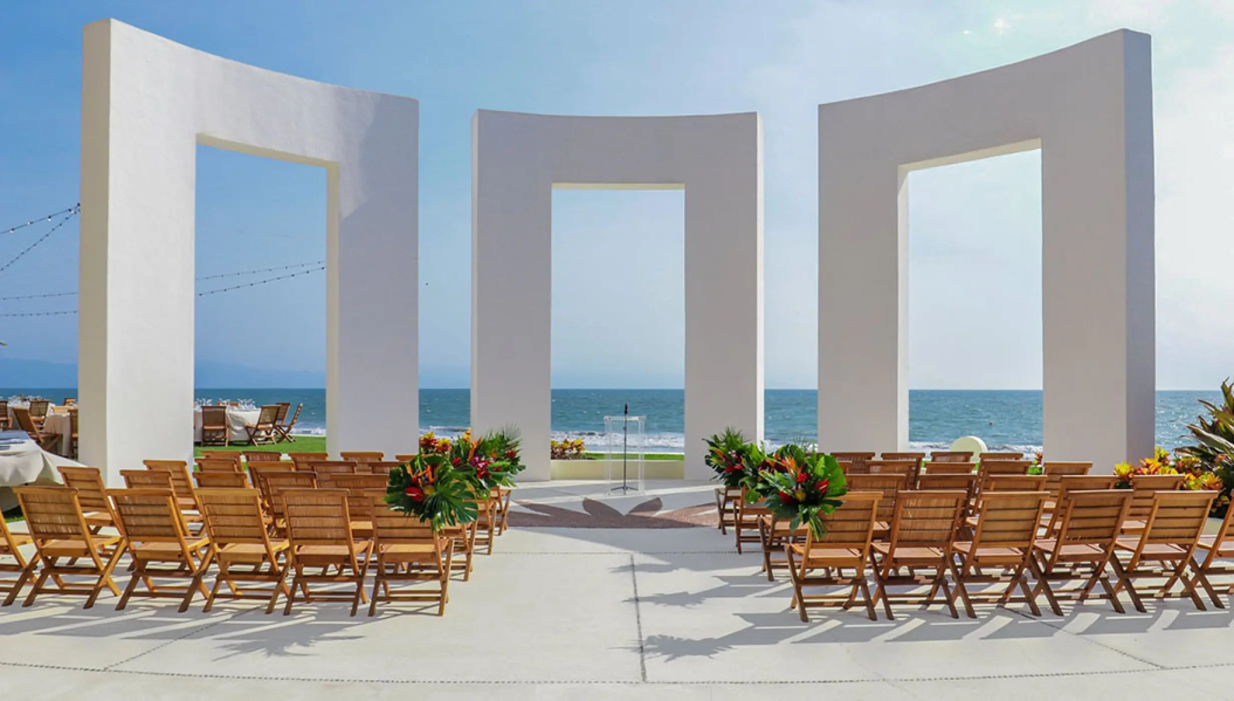 Terrace wedding ceremony with wooden chairs and white arches at Grand Velas Riviera Nayarit, Puerto Vallarta
