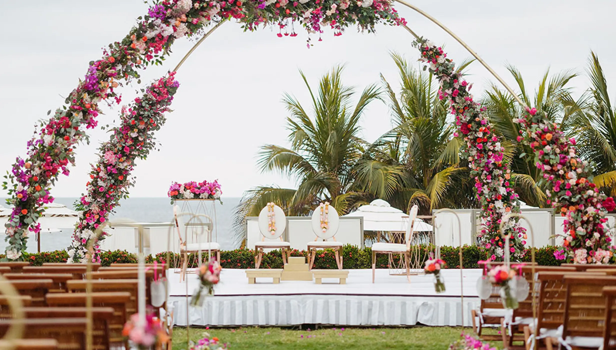 Oceanfront wedding ceremony setup with a floral arch and wooden chairs at Grand Velas Riviera Nayarit