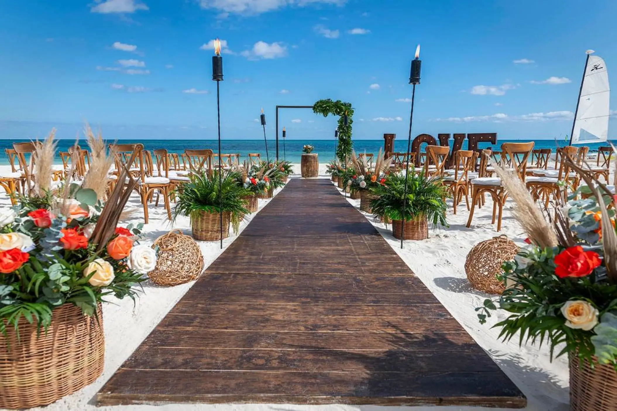 Beachfront wedding ceremony with wooden aisle and floral decor at Ocean Maya Royale, Riviera Maya