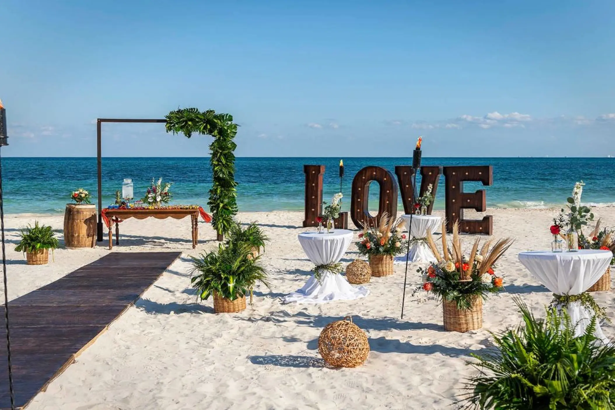 Beachfront wedding ceremony with wooden arch and LOVE sign at Ocean Maya Royale, Riviera Maya
