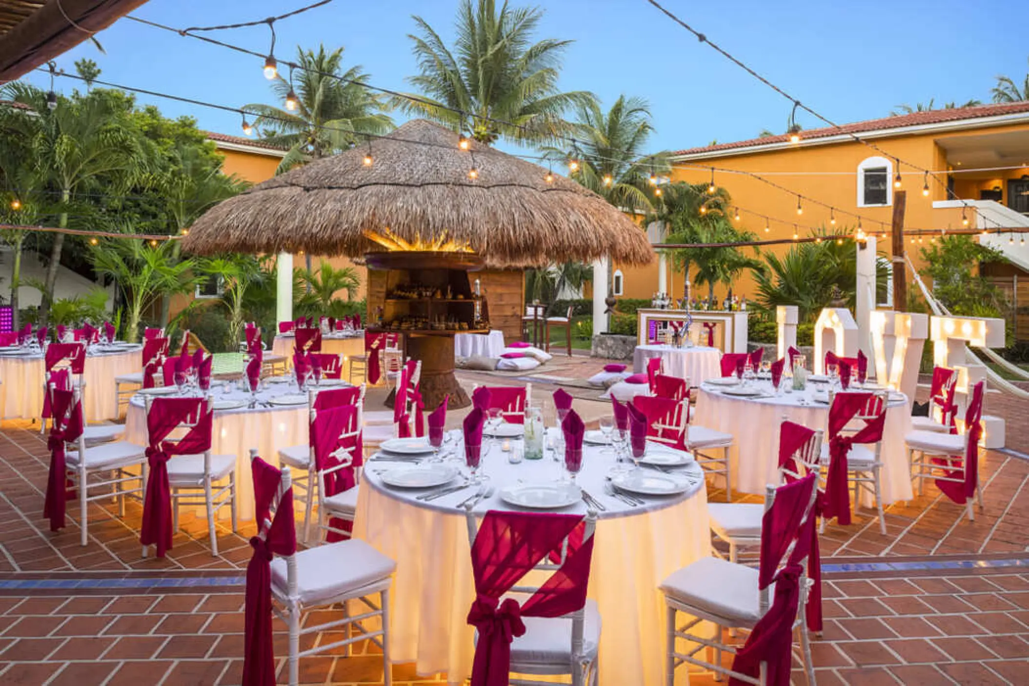 Outdoor wedding reception with magenta chair sashes and string lights at Ocean Maya Royale, Riviera Maya