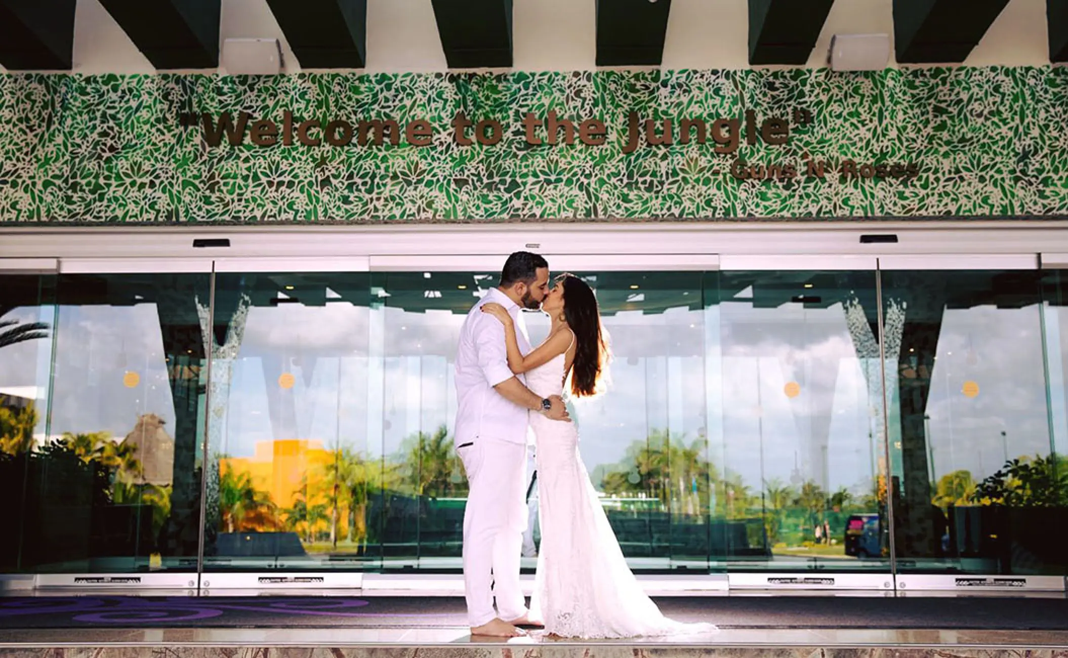 The bride and groom kissing in front of the Welcome to the Jungle sign at Hard Rock Cancun
