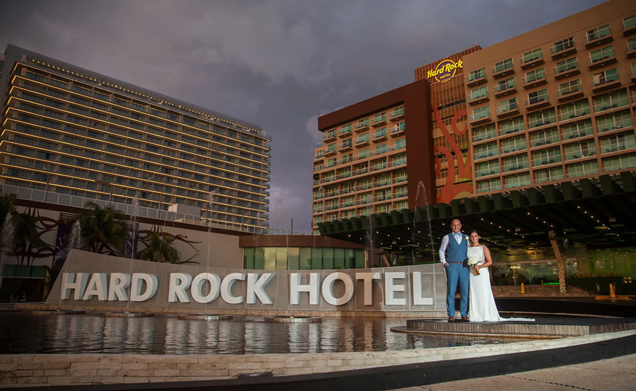 The bride and groom standing by the entrance sign of Hard Rock Cancun at dusk