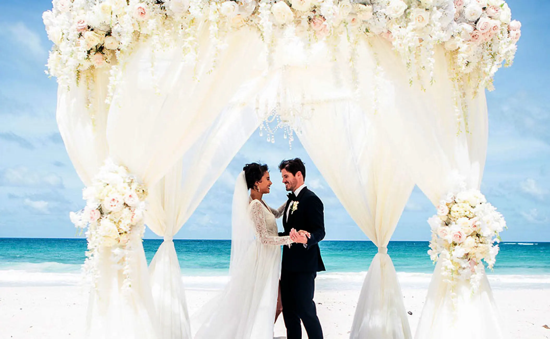 The bride and groom under a floral gazebo for a beach ceremony at Hard Rock Hotel Vallarta, Puerto Vallarta