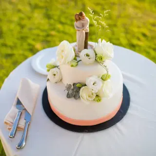 Two-tier white wedding cake with floral accents and couple topper at Hard Rock Vallarta