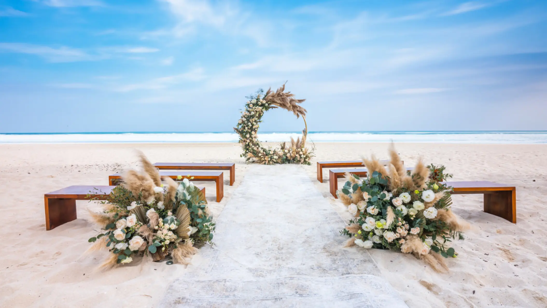Beachfront wedding ceremony setup with floral hoop and wooden benches at Hilton Cancun Mar Caribe, Cancun