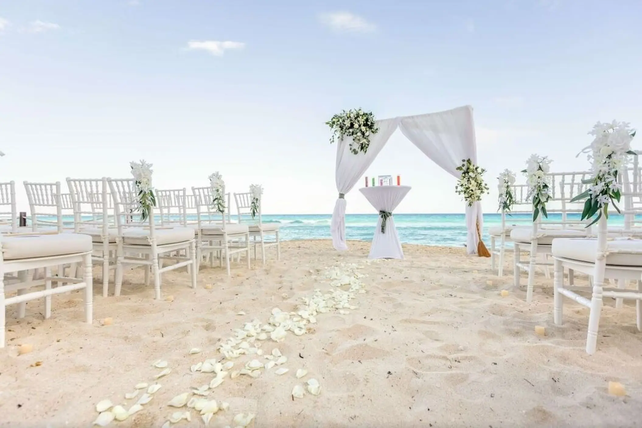 Beachfront wedding ceremony setup with white chairs and floral arch at Hilton Cancun Mar Caribe, Cancun