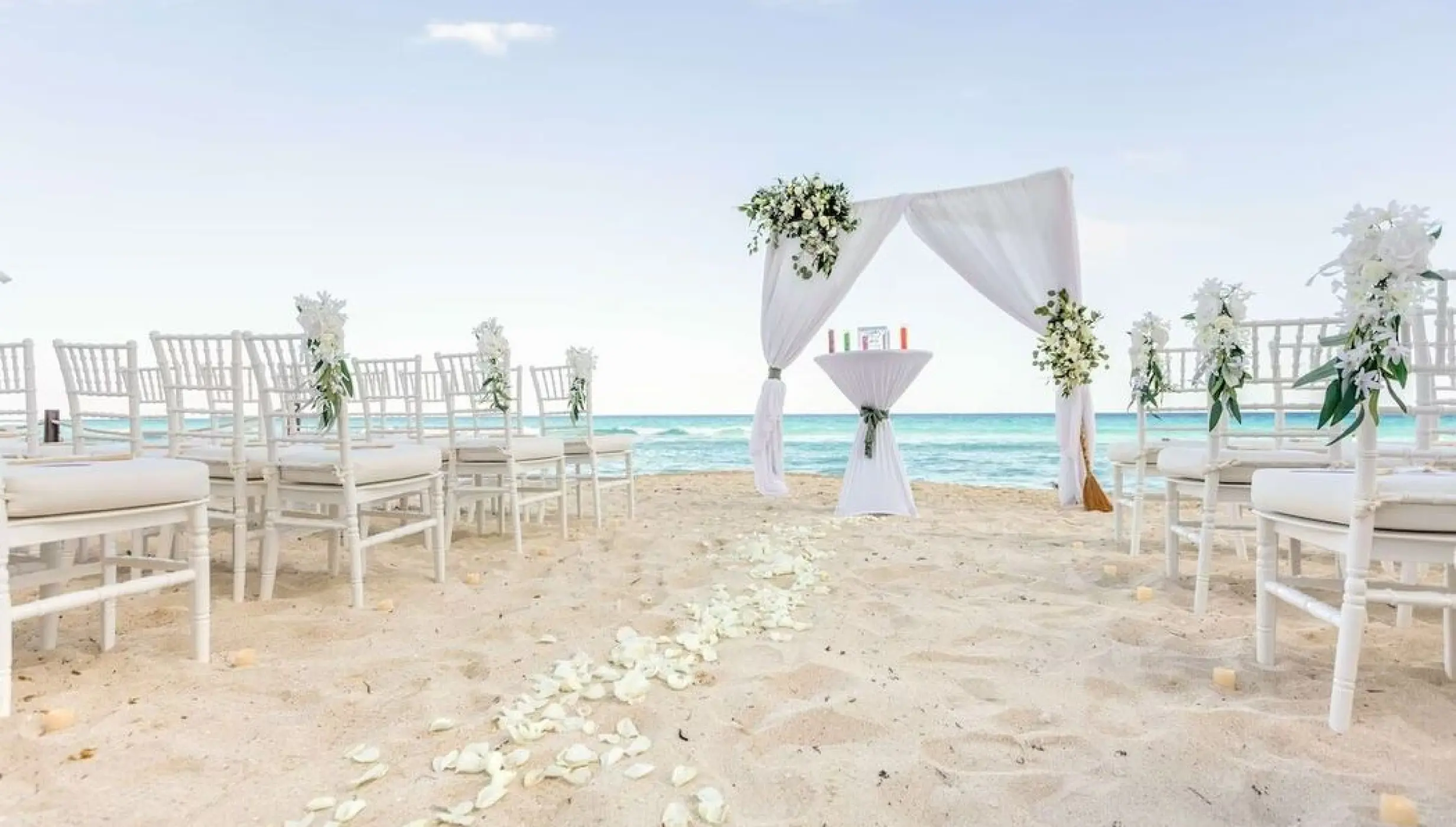 Beachfront wedding ceremony setup with white chairs and floral arch at Hilton Cancun Mar Caribe, Cancun