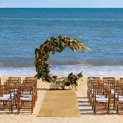 Beachfront wedding ceremony with a circular floral arch and wooden chairs at Hilton Cancun, Cancun