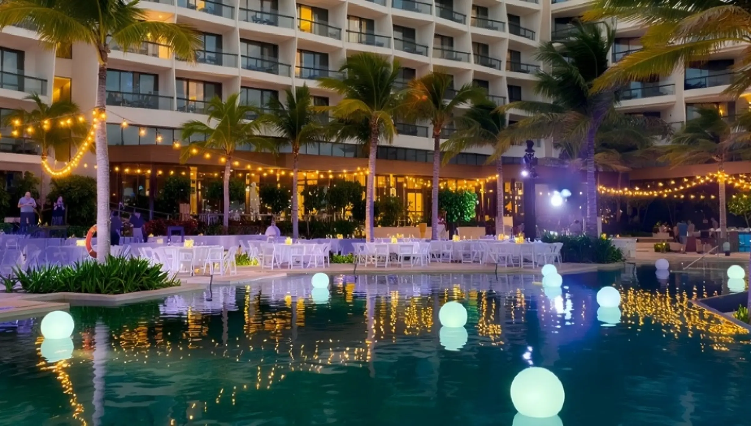 Evening wedding reception at Hilton Cancun with white tables and floating lights in the South Pool, Cancun