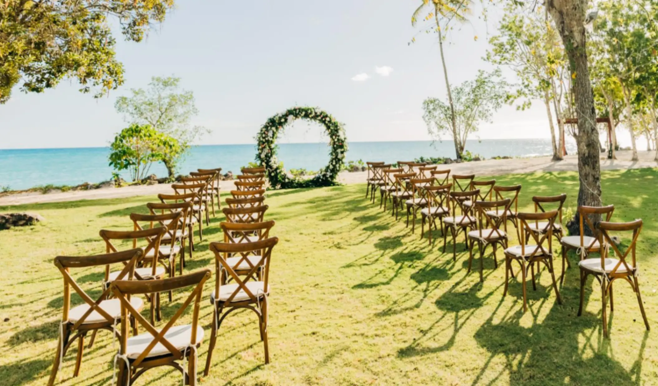 Garden wedding ceremony setup with floral hoop arch and wooden chairs at Hilton La Romana