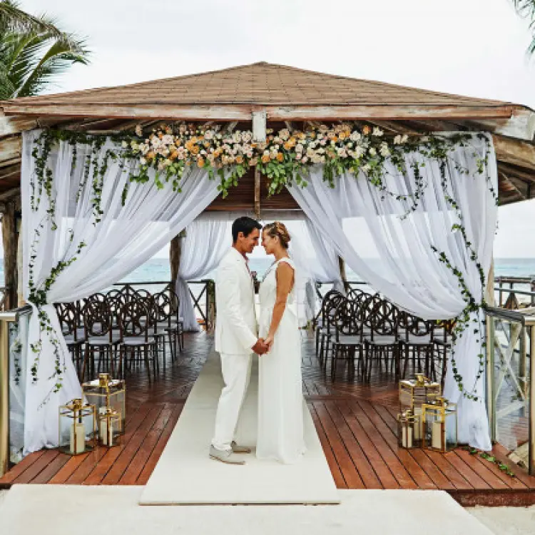 The couple holding hands under a decorated wooden wedding gazebo at Hyatt Zilara Cancun