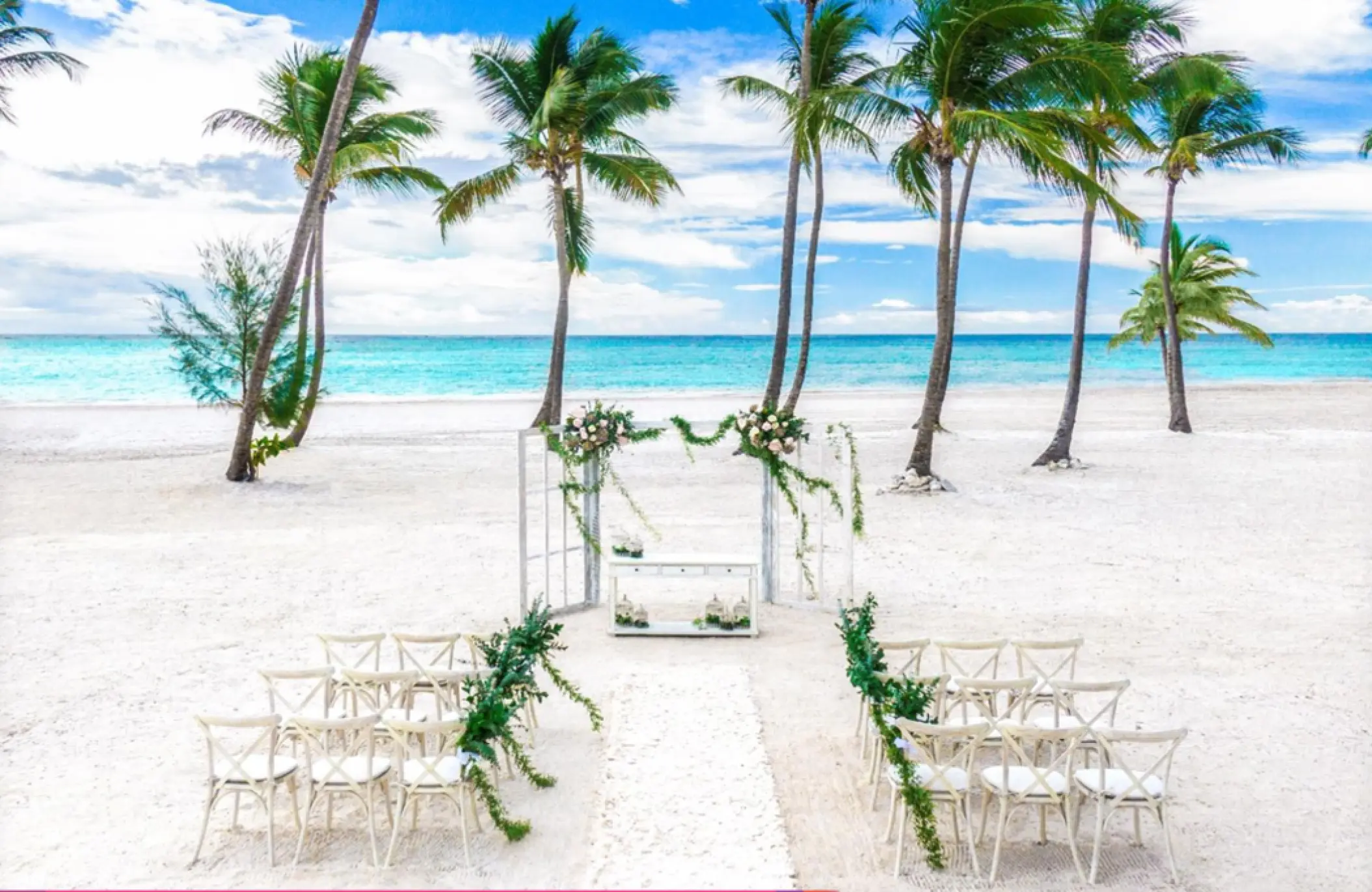 Beachfront wedding ceremony with white chairs and floral arch at Hyatt Zilara Cap Cana, Punta Cana