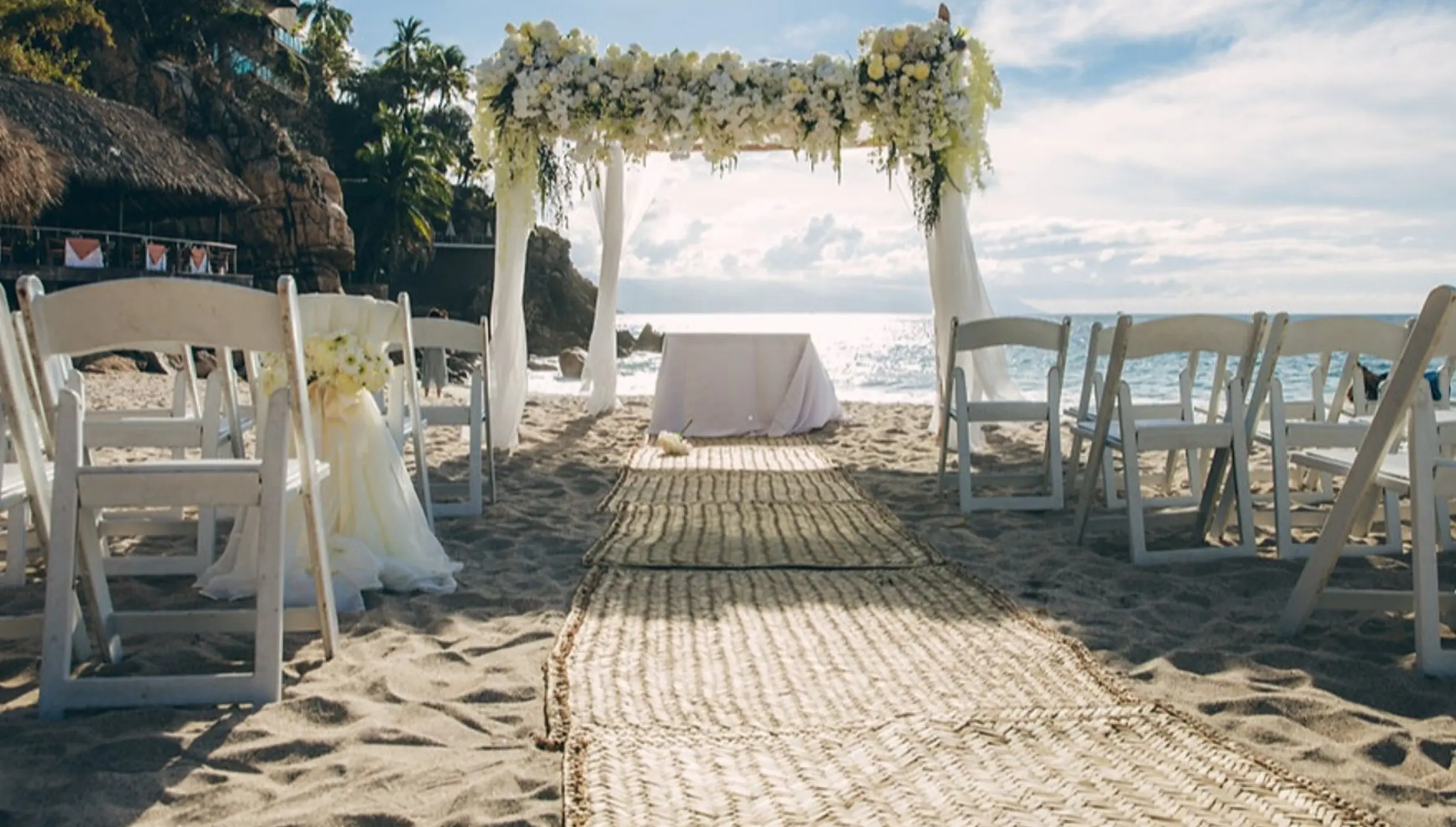 Beachfront wedding ceremony with floral chuppah and straw runner at Hyatt Ziva Puerto Vallarta