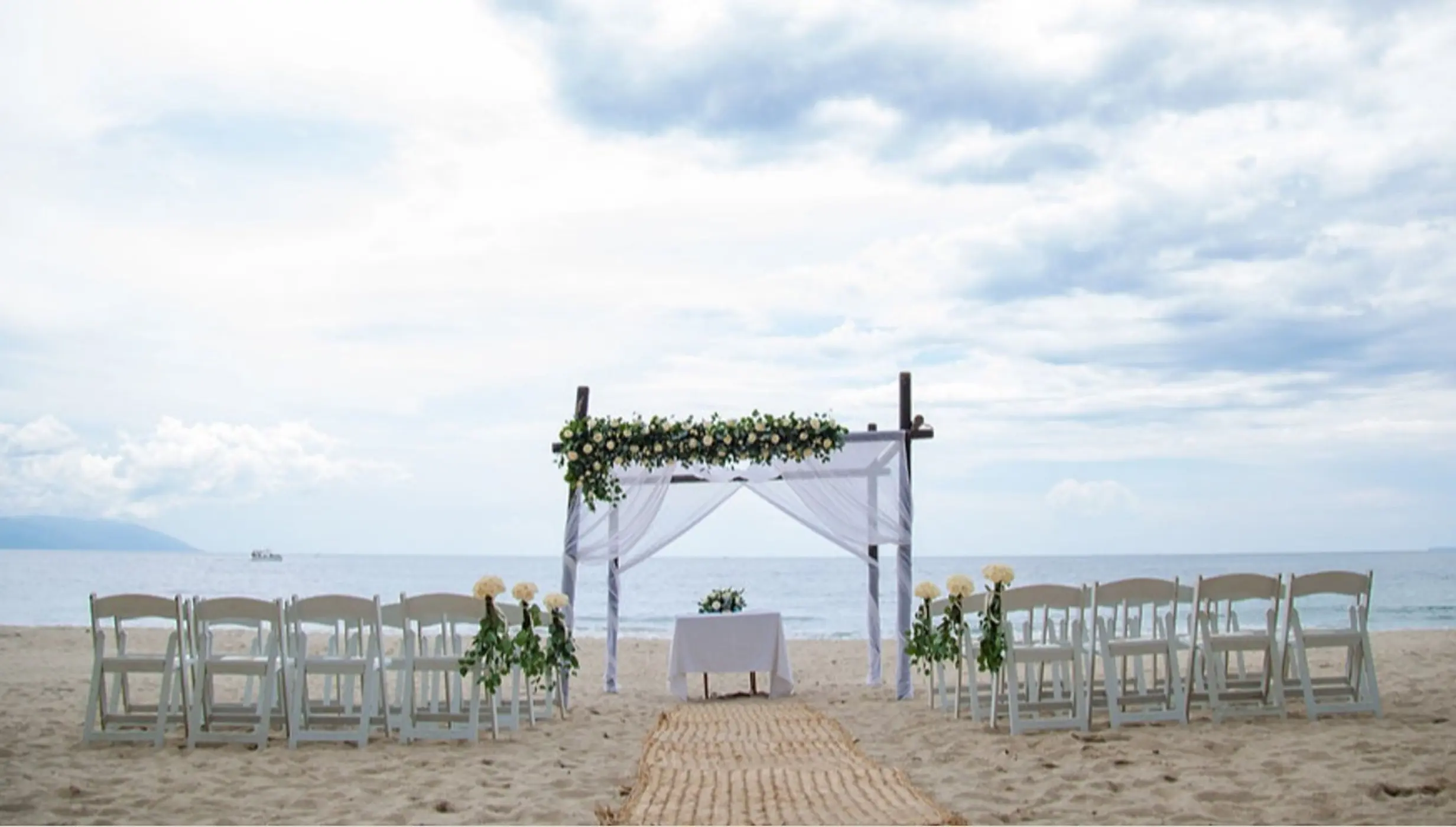 Beachfront wedding ceremony setup with white chairs and floral arch at Hyatt Ziva Puerto Vallarta
