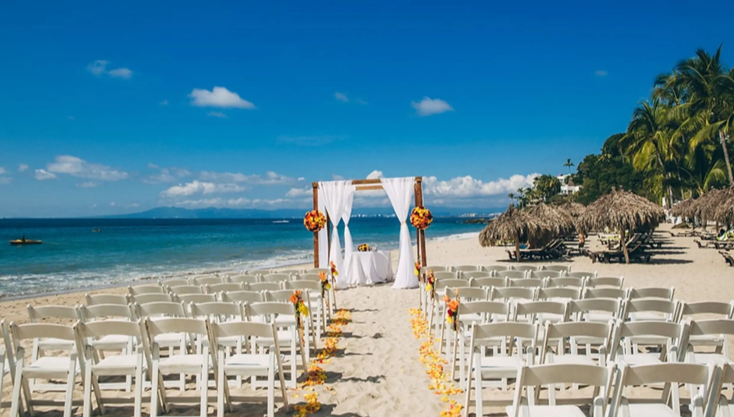 Beach wedding ceremony setup with white chairs and floral arch at Hyatt Ziva Puerto Vallarta