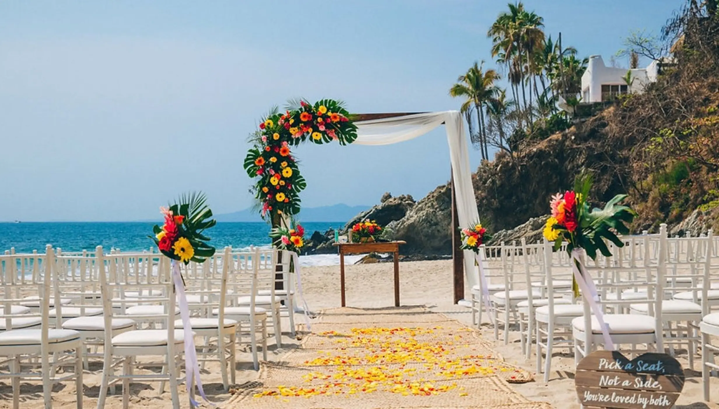 Beachfront wedding ceremony with floral arch and white chairs at Hyatt Ziva Puerto Vallarta