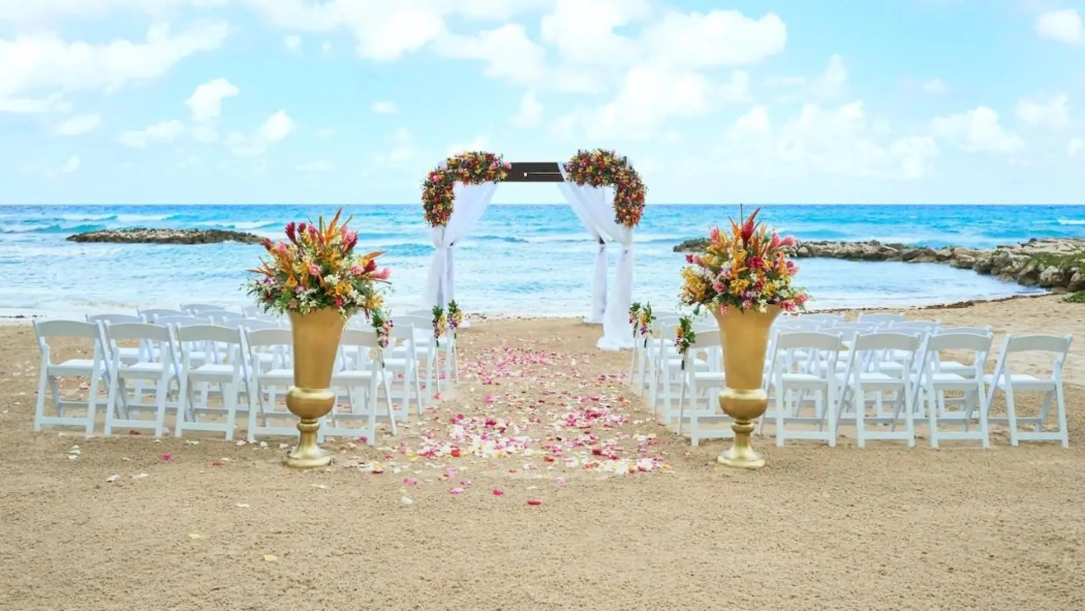 Beachfront wedding ceremony with white chairs and floral arch at Hyatt Ziva Rose Hall, Montego Bay