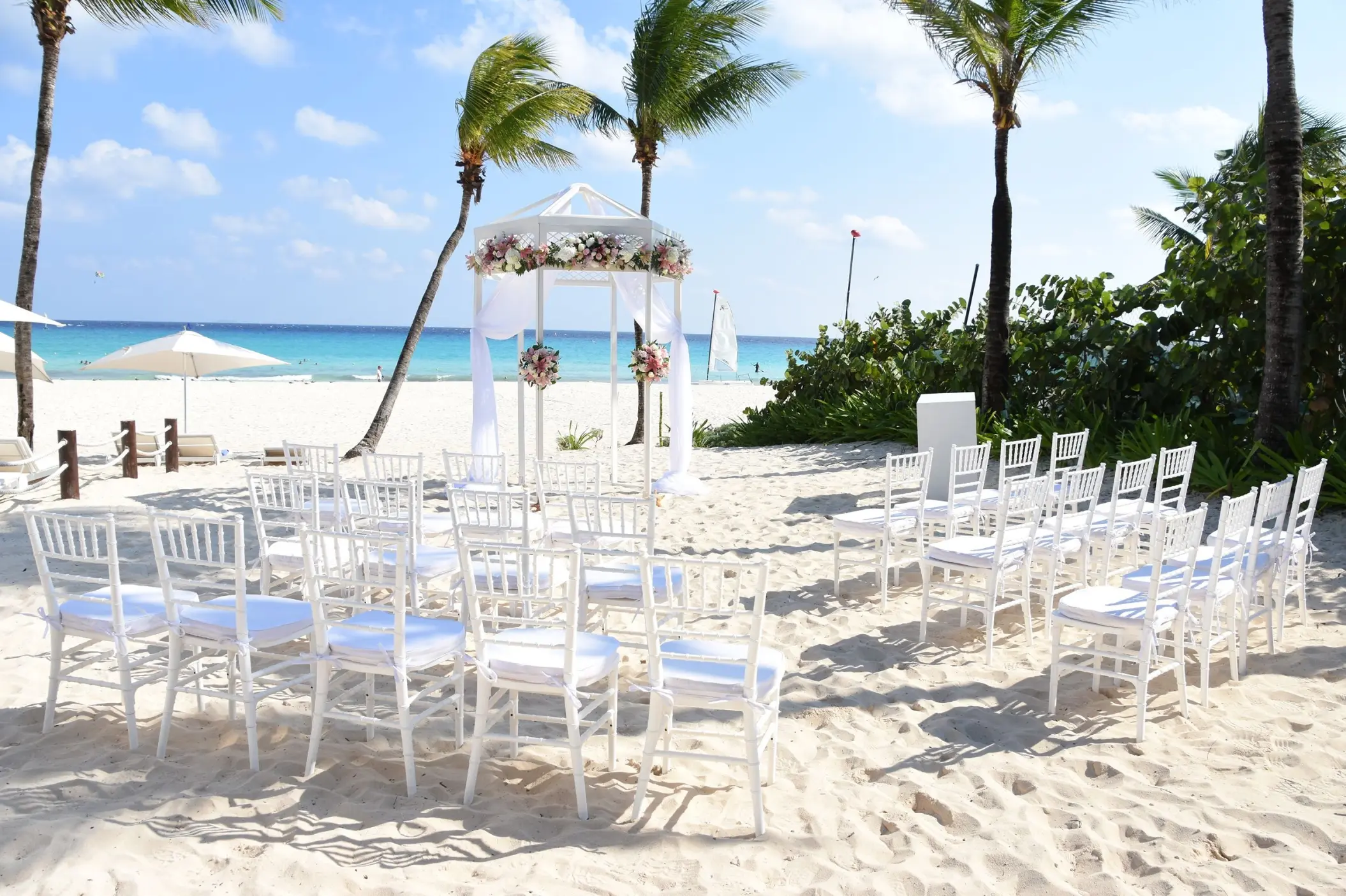 Beachfront wedding ceremony setup with white chairs and a floral gazebo at Iberostar Waves Quetzal, Playa Del Carmen