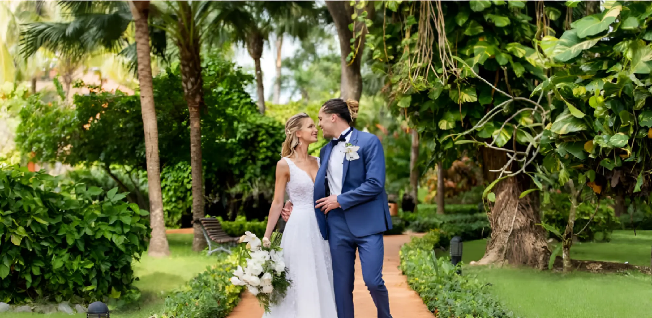 Bride and groom standing on a tropical garden path at Iberostar Selection Hacienda Dominicus, La Romana