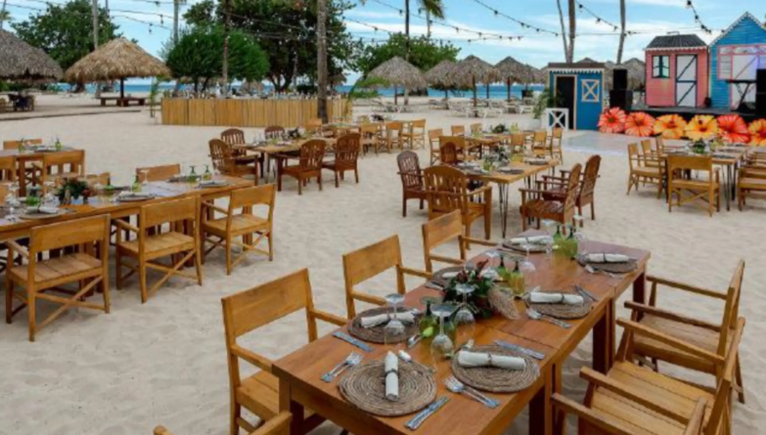 Beachfront wedding reception setup with wooden tables and a colorful stage at Iberostar Selection Hacienda Dominicus, La Romana