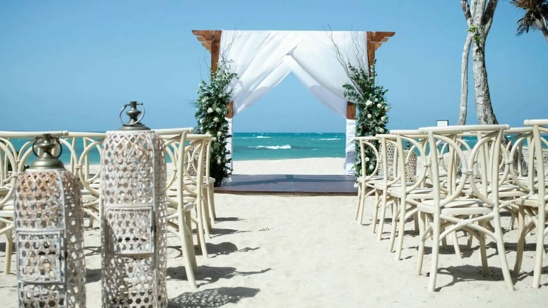 Beachfront wedding ceremony with white fabric arch and lanterns at Iberostar Waves Costa Dorada, Puerto Plata
