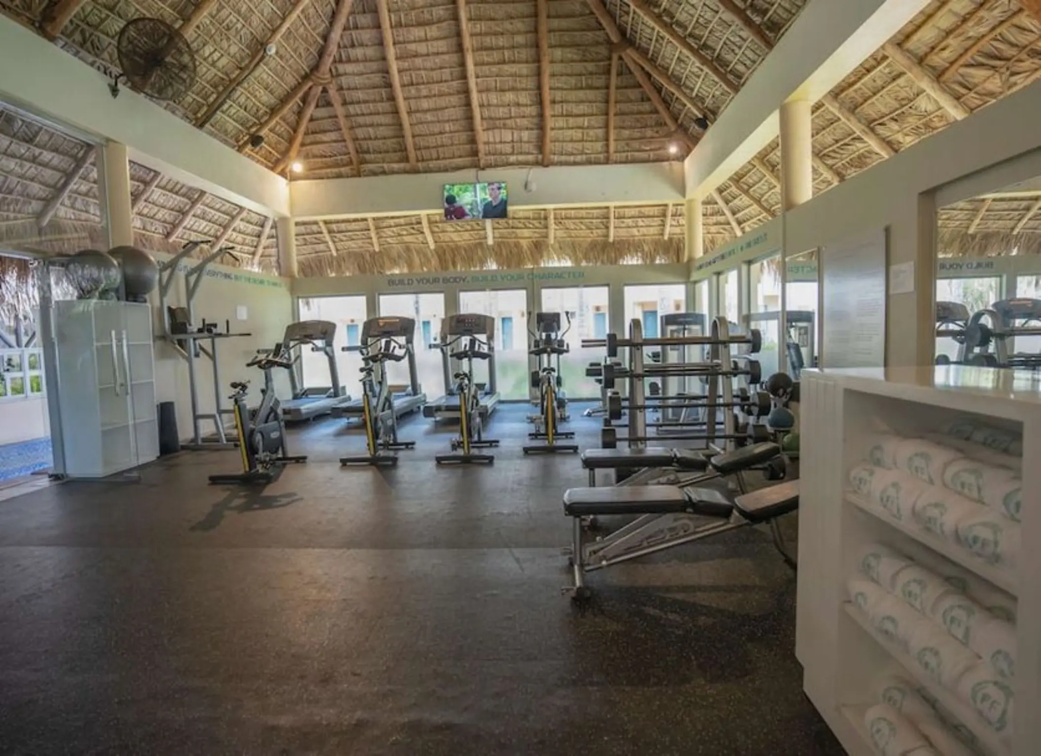 Fitness center with exercise bikes and weight machines under a thatched roof at Iberostar Costa Dorada, Puerto Plata