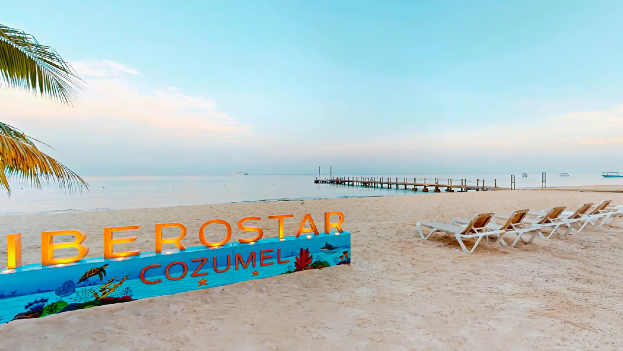 Iberostar Waves Cozumel sign and lounge chairs on the beach at sunset, Cozumel