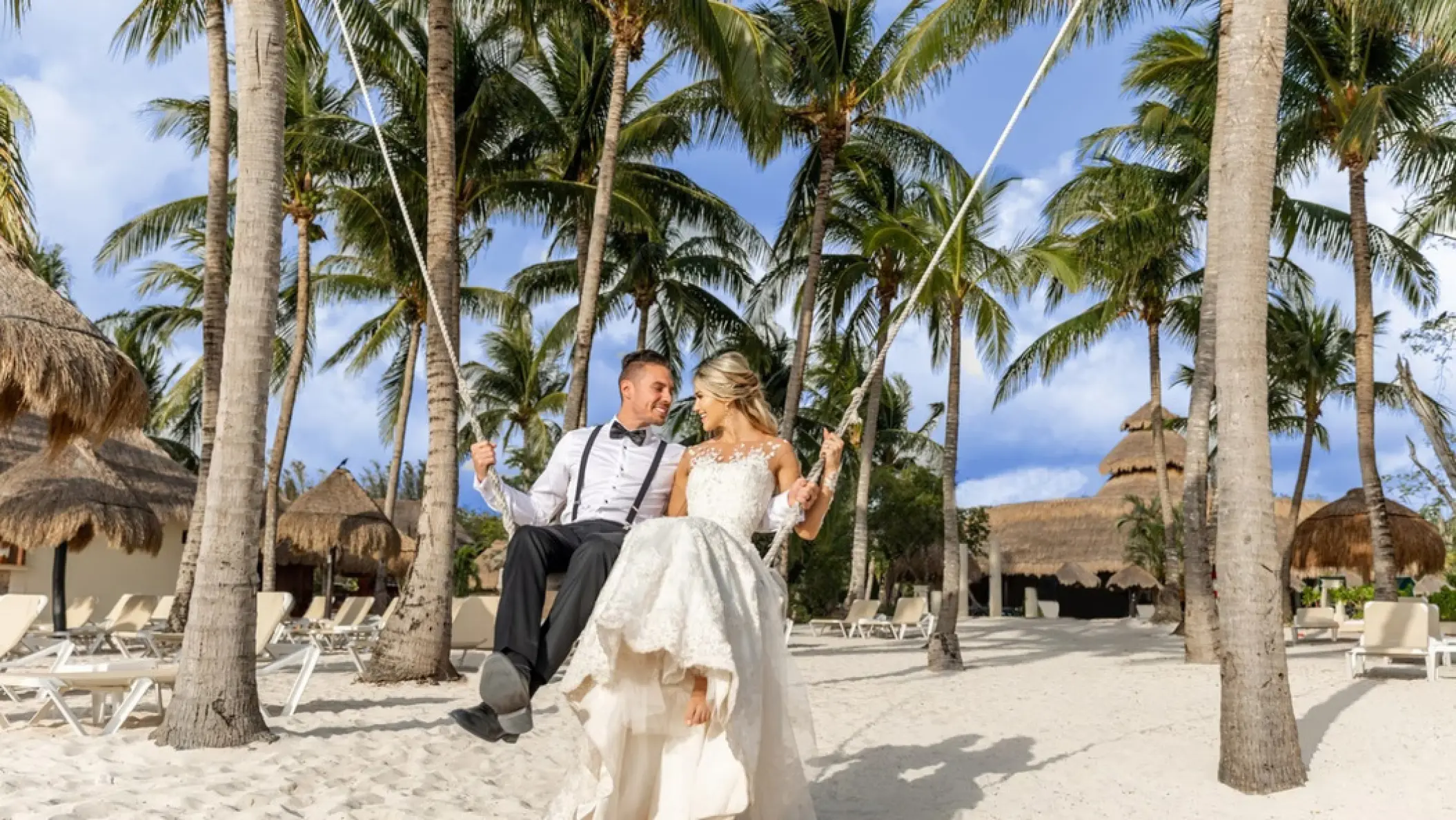 Bride and groom sitting on a beach swing among palm trees at Iberostar Waves Cozumel