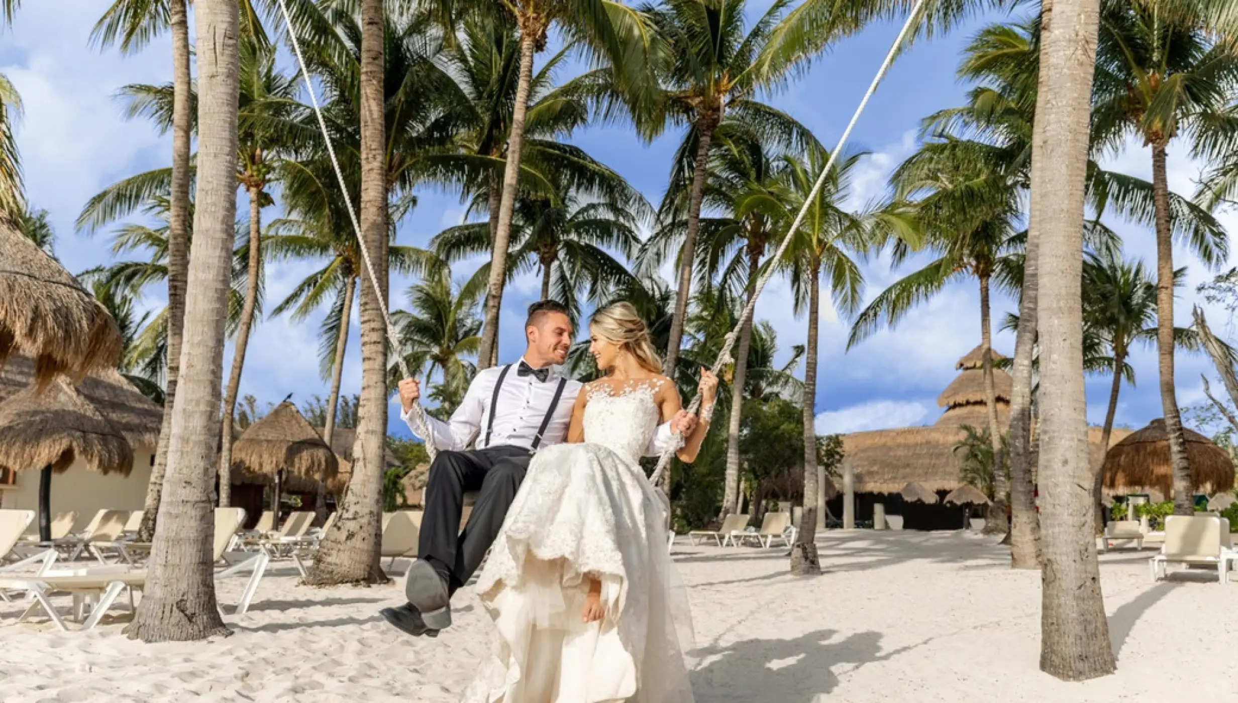Bride and groom sitting on a beach swing among palm trees at Iberostar Waves Cozumel