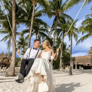 Bride and groom sitting on a beach swing among palm trees at Iberostar Waves Cozumel