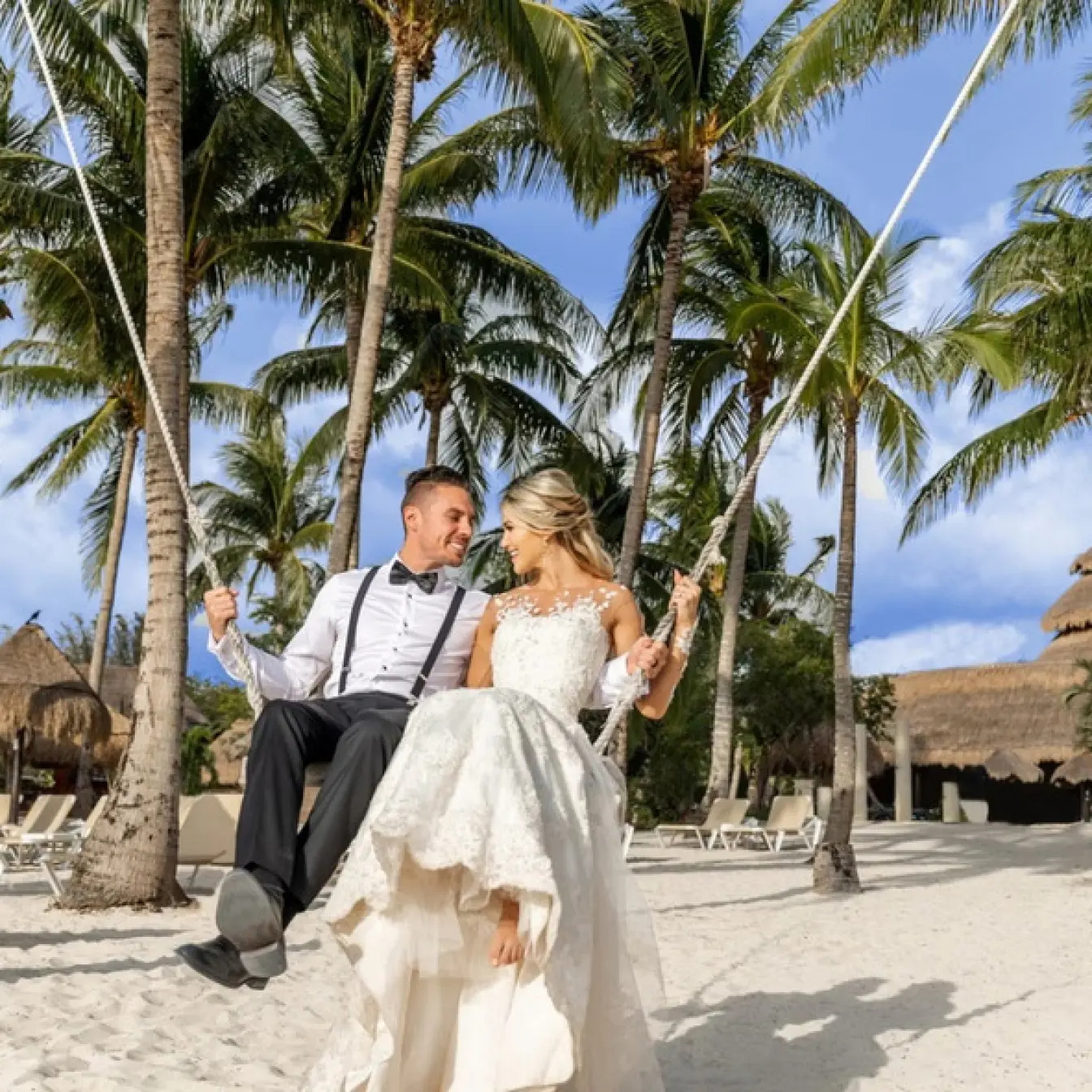 Bride and groom sitting on a beach swing among palm trees at Iberostar Waves Cozumel