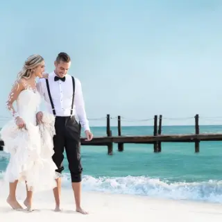 Bride and groom walking barefoot along the beach at Iberostar Waves Cozumel