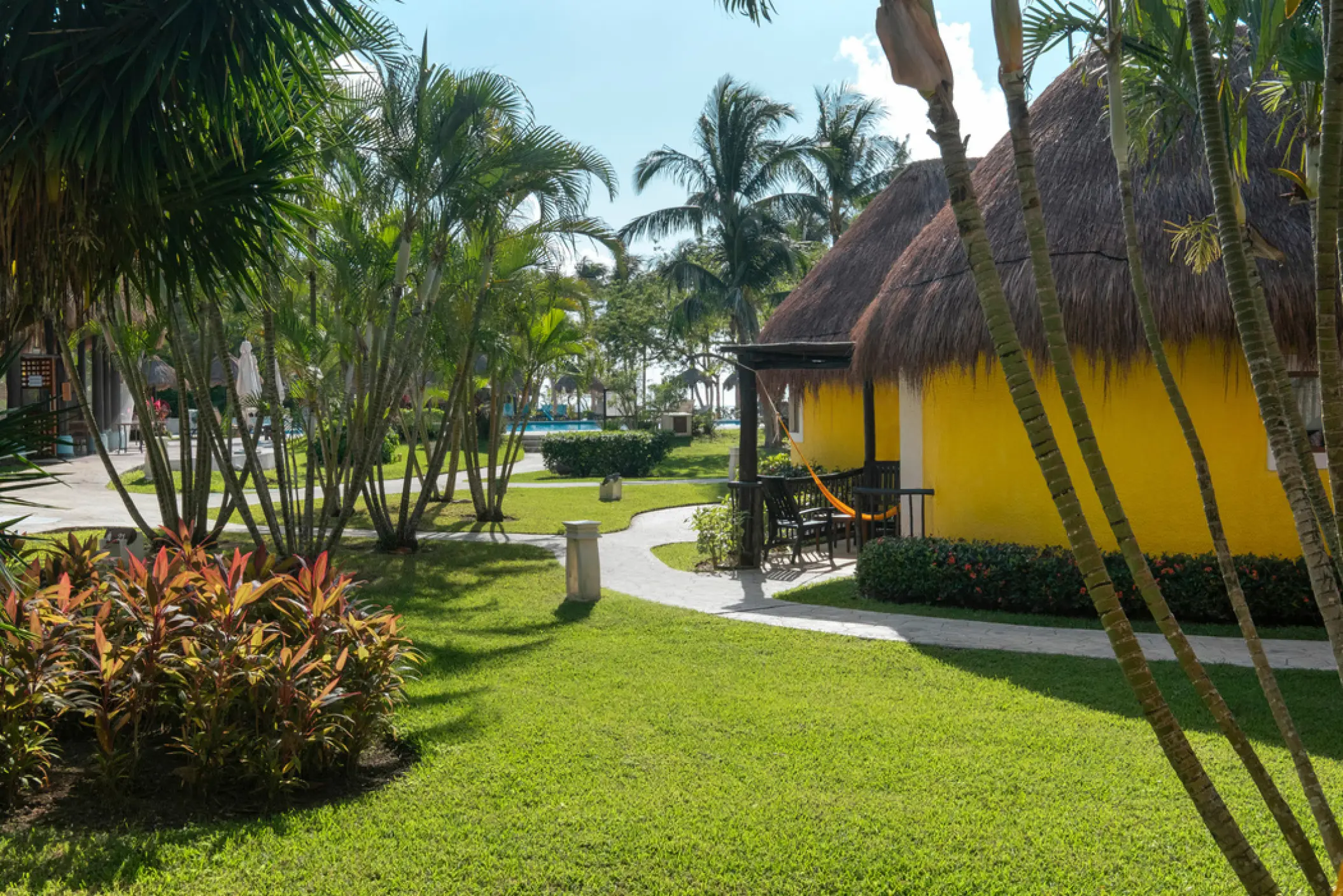 Yellow bungalow suites with thatched roofs and garden pathways at Iberostar Waves Cozumel