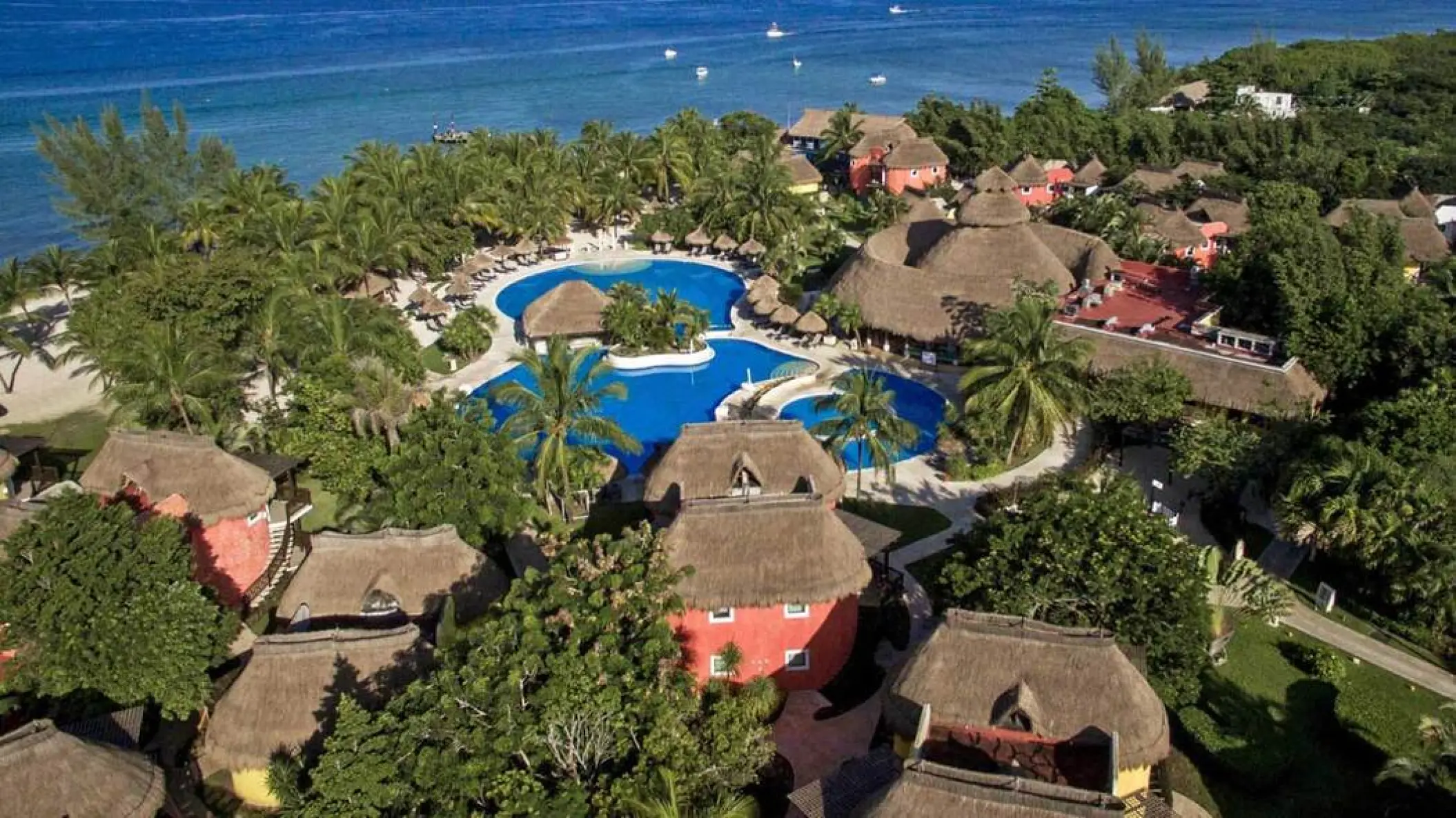 Aerial view of Iberostar Waves Cozumel pools and thatched-roof buildings along the coastline, Cozumel