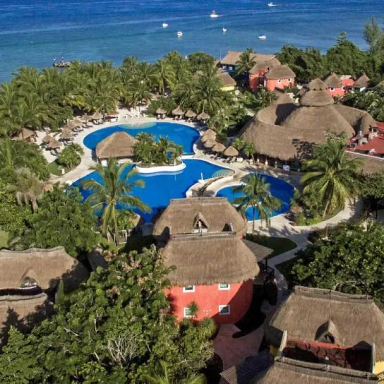 Aerial view of Iberostar Waves Cozumel pools and thatched-roof buildings along the coastline, Cozumel